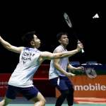 Goh Sze Fei executes a forehand drive while Nur Izzuddin Rumsani covers the back court in their white jerseys.