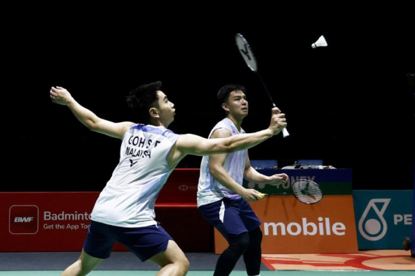 Goh Sze Fei executes a forehand drive while Nur Izzuddin Rumsani covers the back court in their white jerseys.