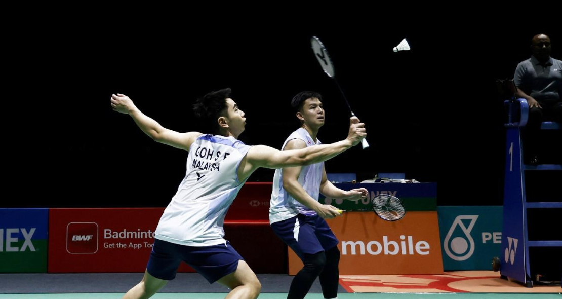 Goh Sze Fei executes a forehand drive while Nur Izzuddin Rumsani covers the back court in their white jerseys.
