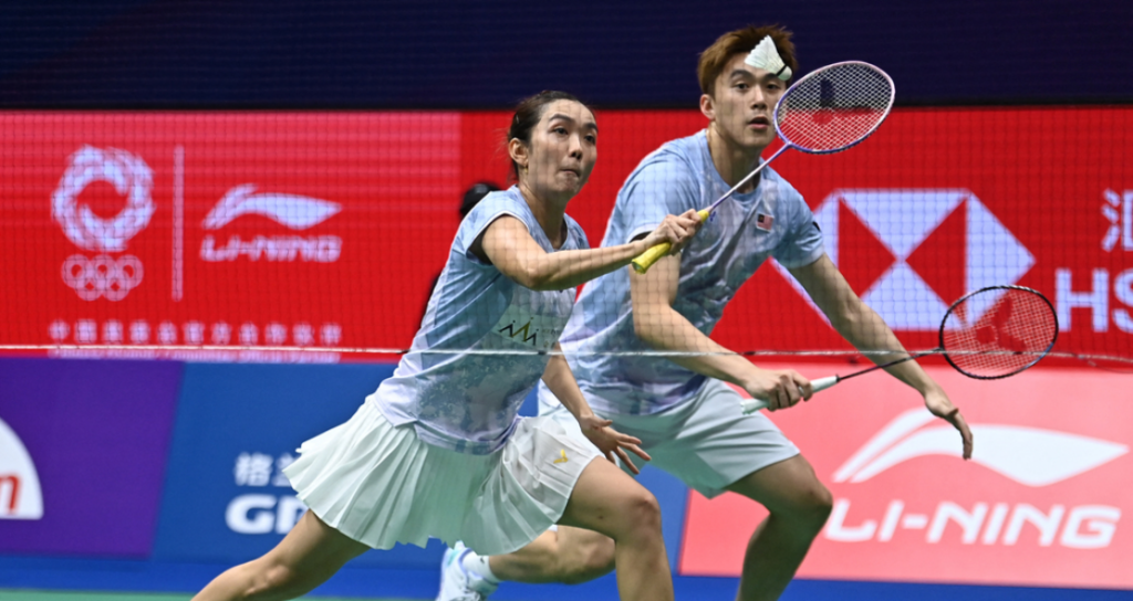 Lai Pei Jing lunges low at the net while Hoo Pang Ron tracks the shuttlecock in their light blue Malaysian jerseys.