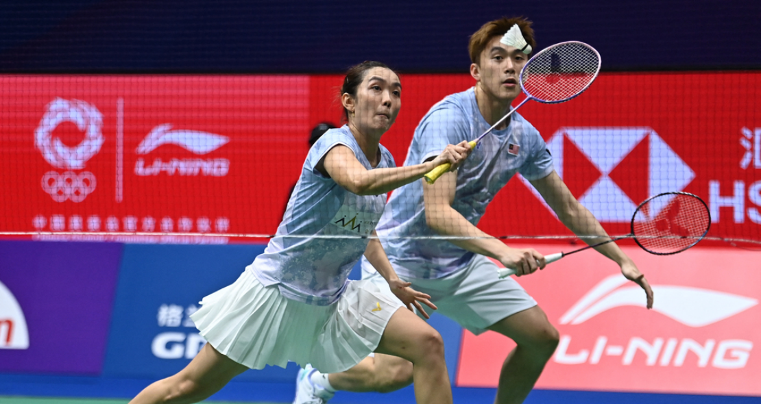Lai Pei Jing lunges low at the net while Hoo Pang Ron tracks the shuttlecock in their light blue Malaysian jerseys.