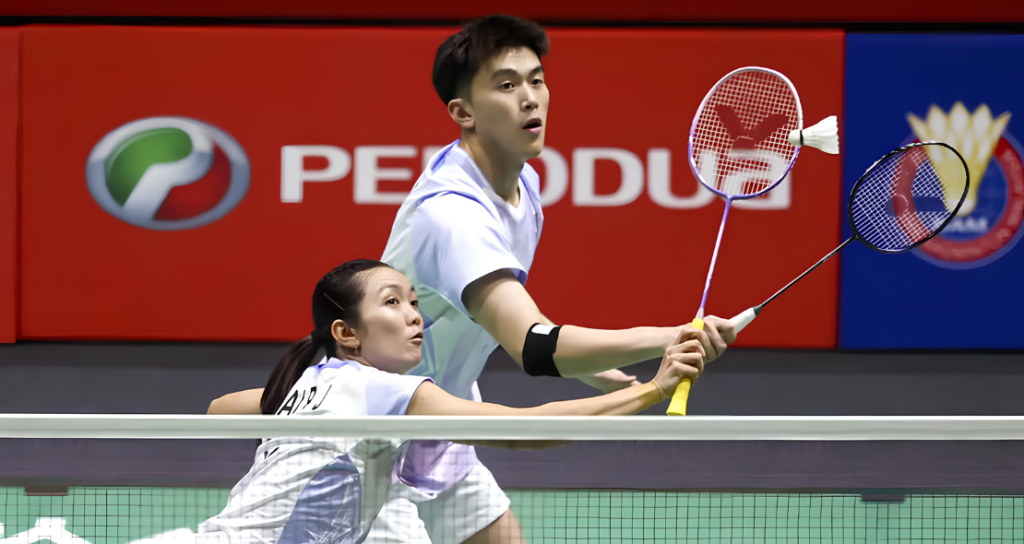 Hoo Pang Ron raises his racket to attack while Lai Pei Jing crouches at the net in their white jerseys.