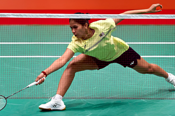 K. Letshanaa lunges deeply forward across the court to play a low net return in her yellow Malaysian national jersey.