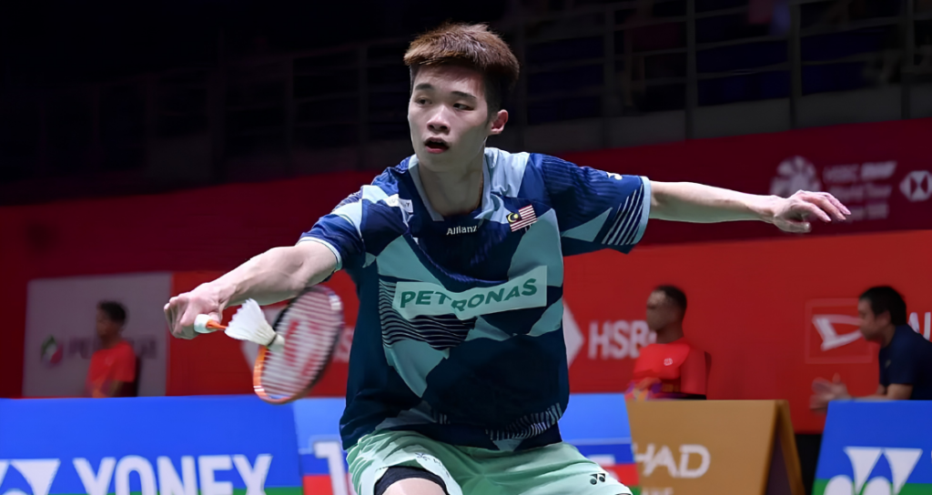 Kong Wei Xiang lunges forward low to play a backhand net shot in his blue Petronas Malaysian jersey.