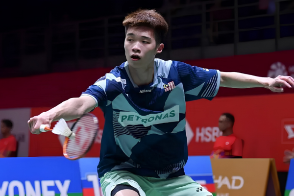 Kong Wei Xiang lunges forward low to play a backhand net shot in his blue Petronas Malaysian jersey.
