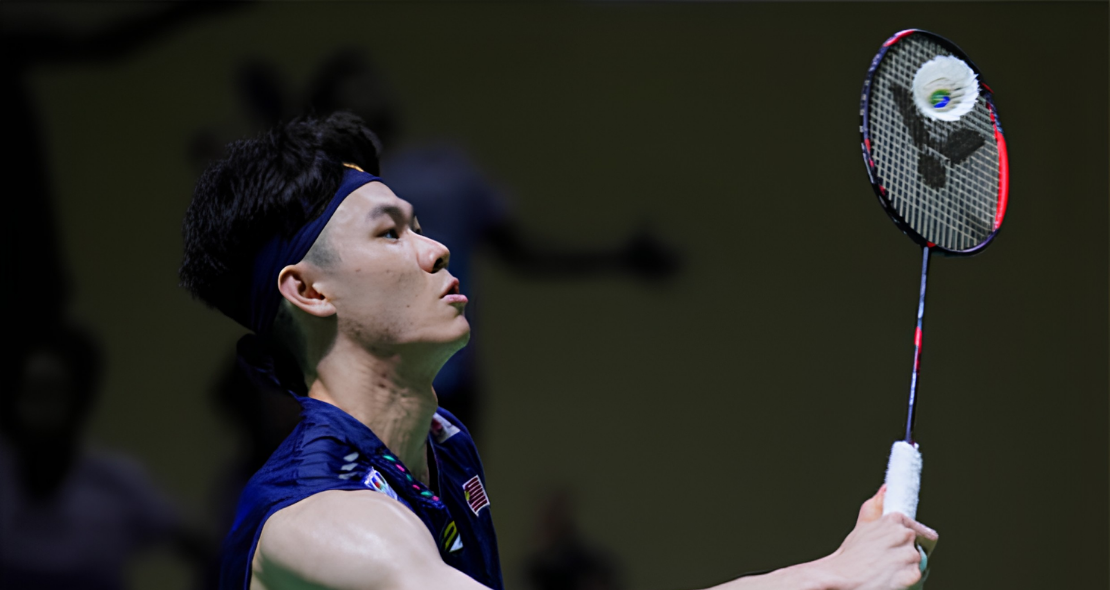 Lee Zii Jia looks up with intense focus as he strikes an overhead shot in his navy Malaysian jersey.