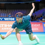 Lee Zii Jia lunges forward low to retrieve the shuttlecock at the net in his teal jersey and blue Victor headband.