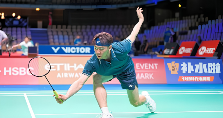 Lee Zii Jia lunges forward low to retrieve the shuttlecock at the net in his teal jersey and blue Victor headband.