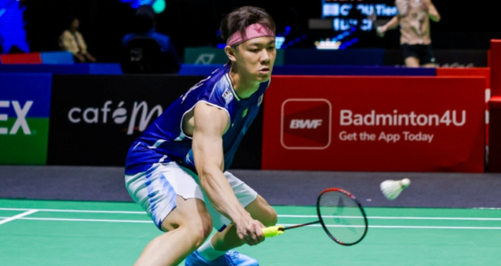 Lee Zii Jia lunges low to execute a delicate forehand return in his blue Malaysian jersey and pink headband.