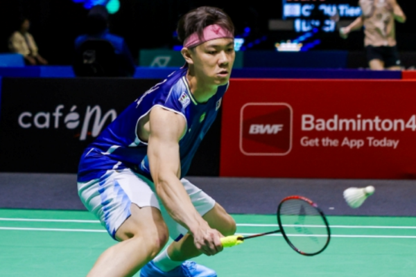 Lee Zii Jia lunges low to execute a delicate forehand return in his blue Malaysian jersey and pink headband.