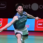 Leong Jun Hao lunges deeply forward across the court to return a shot in his teal Petronas Malaysian jersey.