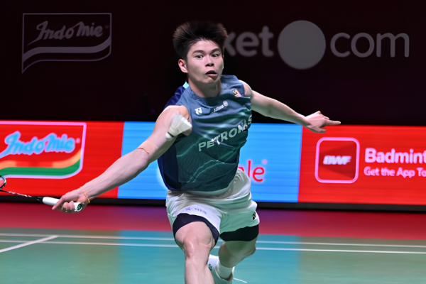 Leong Jun Hao lunges deeply forward across the court to return a shot in his teal Petronas Malaysian jersey.