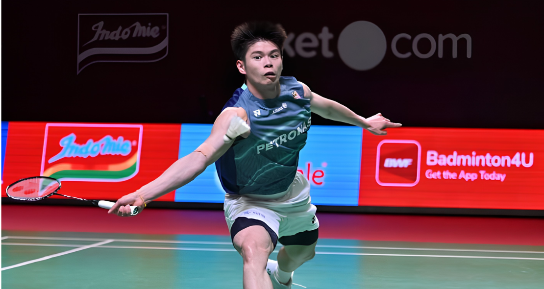 Leong Jun Hao lunges deeply forward across the court to return a shot in his teal Petronas Malaysian jersey.