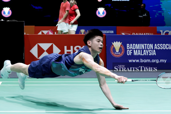 Leong Jun Hao executes a full horizontal dive across the court to retrieve the shuttlecock in his blue Petronas jersey.