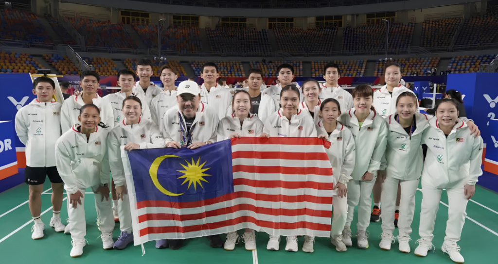The Malaysian World Junior badminton squad and team manager Vincent Chin pose with the national flag on court in Cairo.