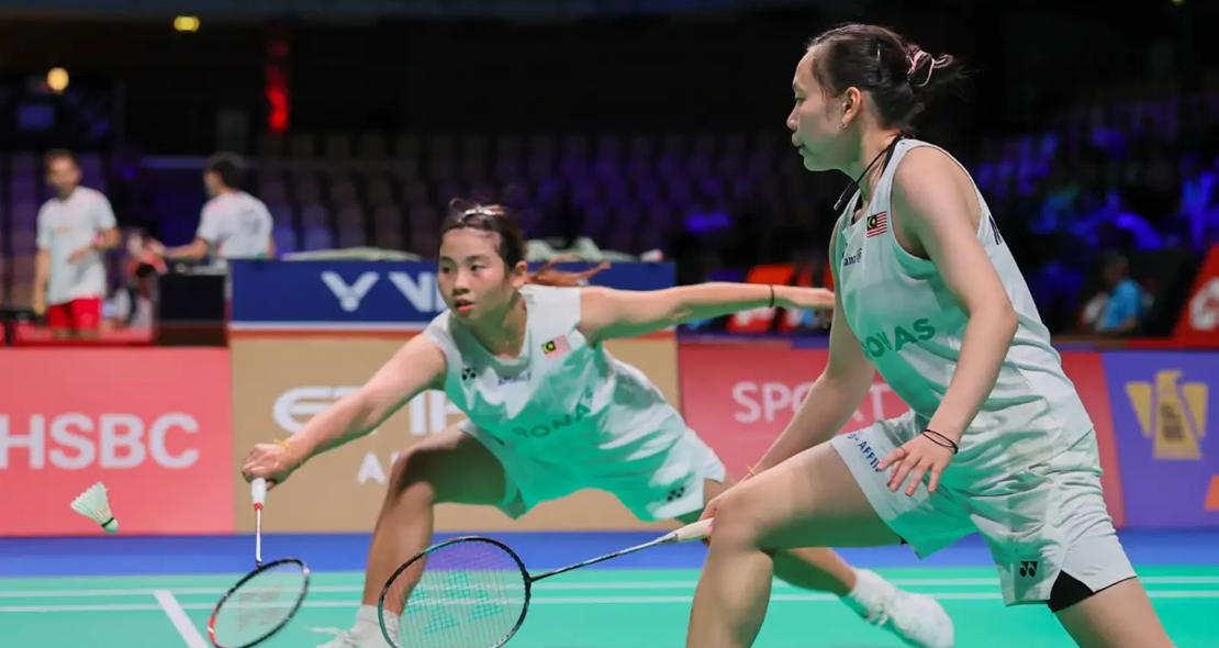 Ong Xin Yee lunges low to return a shot while Carmen Ting stays in ready position in their white Petronas jerseys.