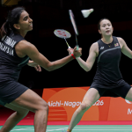 M. Thinaah intercepts the shuttlecock at the net while Pearly Tan adopts a wide defensive ready stance in their black Malaysian jerseys.
