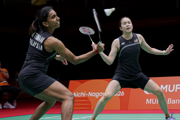 M. Thinaah intercepts the shuttlecock at the net while Pearly Tan adopts a wide defensive ready stance in their black Malaysian jerseys.