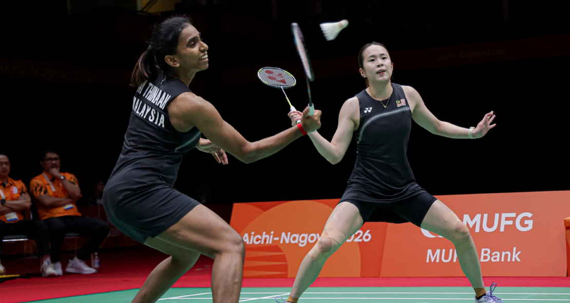 M. Thinaah intercepts the shuttlecock at the net while Pearly Tan adopts a wide defensive ready stance in their black Malaysian jerseys.