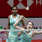 Pearly Tan prepares to intercept the shuttlecock at the net while M. Thinaah covers the back court in their turquoise Malaysian jerseys.