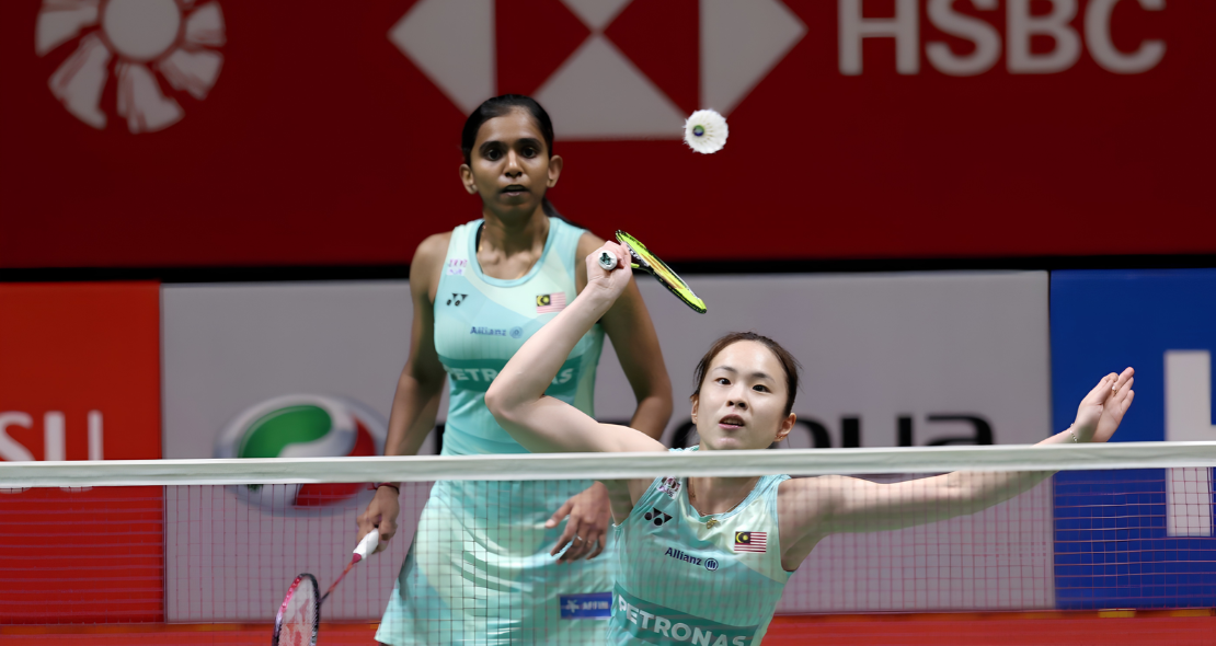 Pearly Tan prepares to intercept the shuttlecock at the net while M. Thinaah covers the back court in their turquoise Malaysian jerseys.