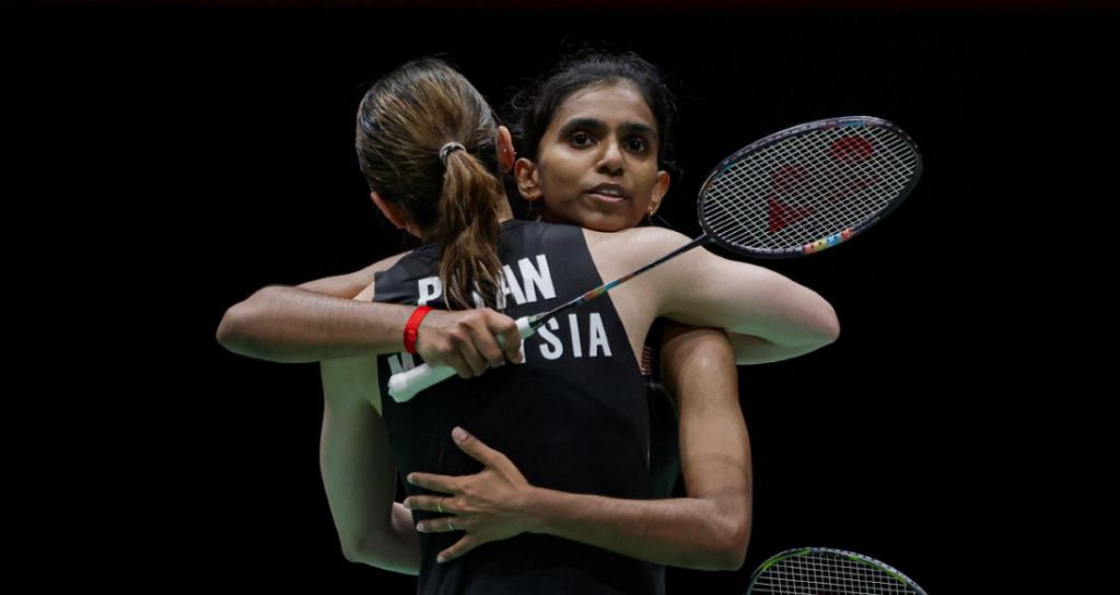 Pearly Tan and M. Thinaah share an emotional embrace on court while holding their rackets in their black Malaysian jerseys.