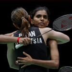 Pearly Tan and M. Thinaah share an emotional embrace on court while holding their rackets in their black Malaysian jerseys.