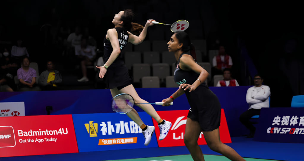 Pearly Tan leaps high in mid-air to smash while M. Thinaah guards the front court in their black Malaysian jerseys.