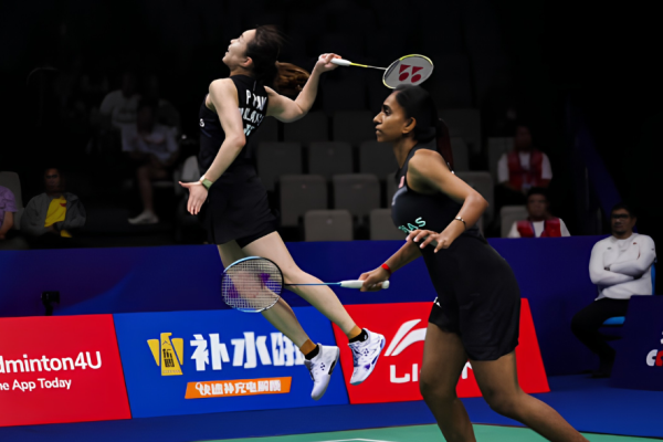 Pearly Tan leaps high in mid-air to smash while M. Thinaah guards the front court in their black Malaysian jerseys.