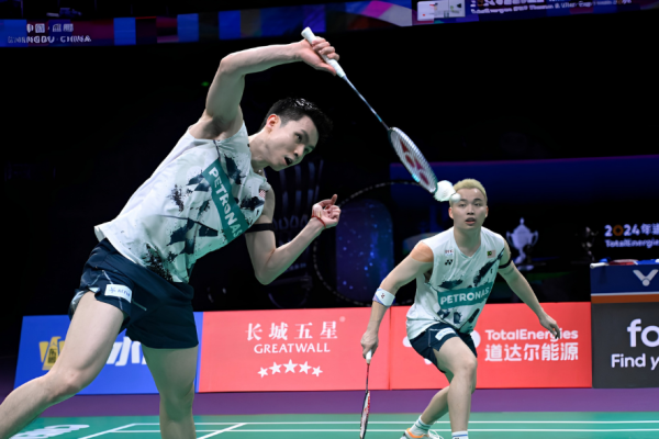 Soh Wooi Yik executes an overhead return while partner Aaron Chia covers the court in their white Petronas jerseys.
